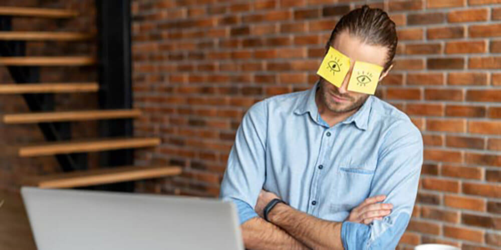 A man sleeping at his desk with sticky notes covering his eyes.