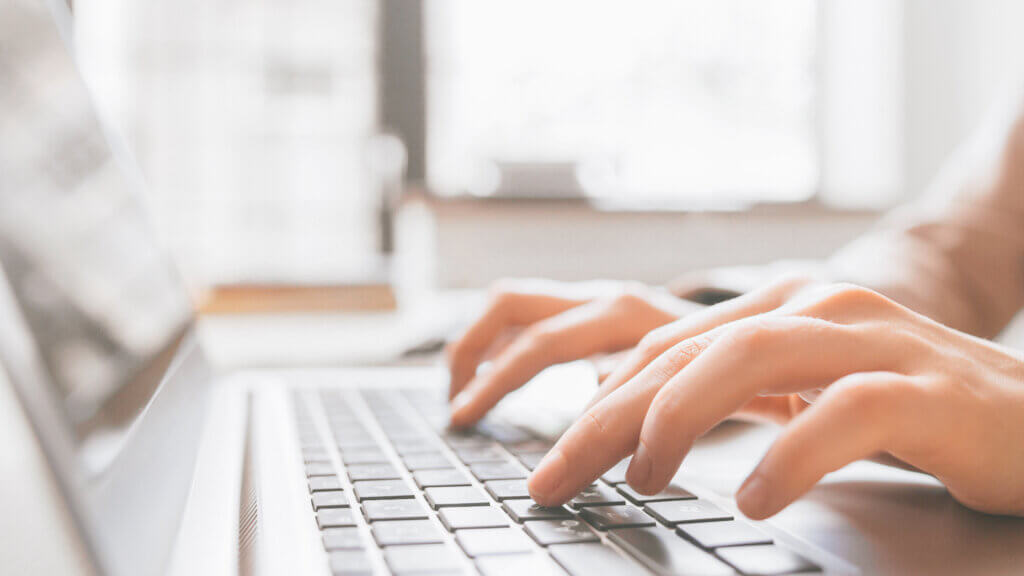 Hands typing on laptop keyboard in bright office setting