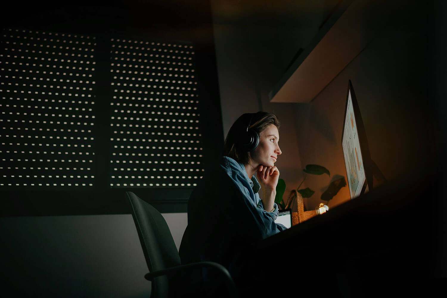 A young woman sitting in her cozy office space with headphones, fully immersed in her computer work.