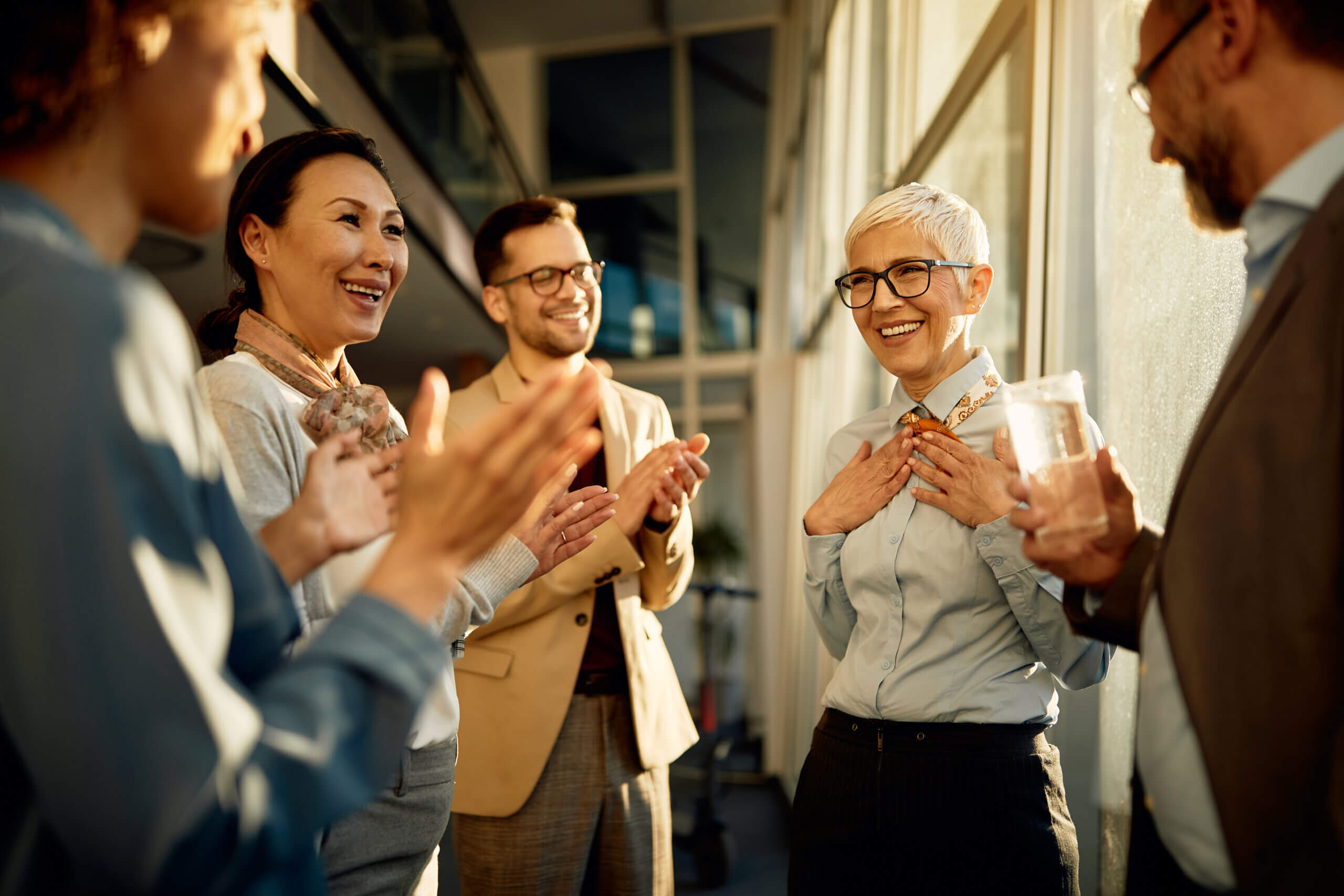 Happy female business leader getting recognition acknowledgement and applause from her business team in the office.