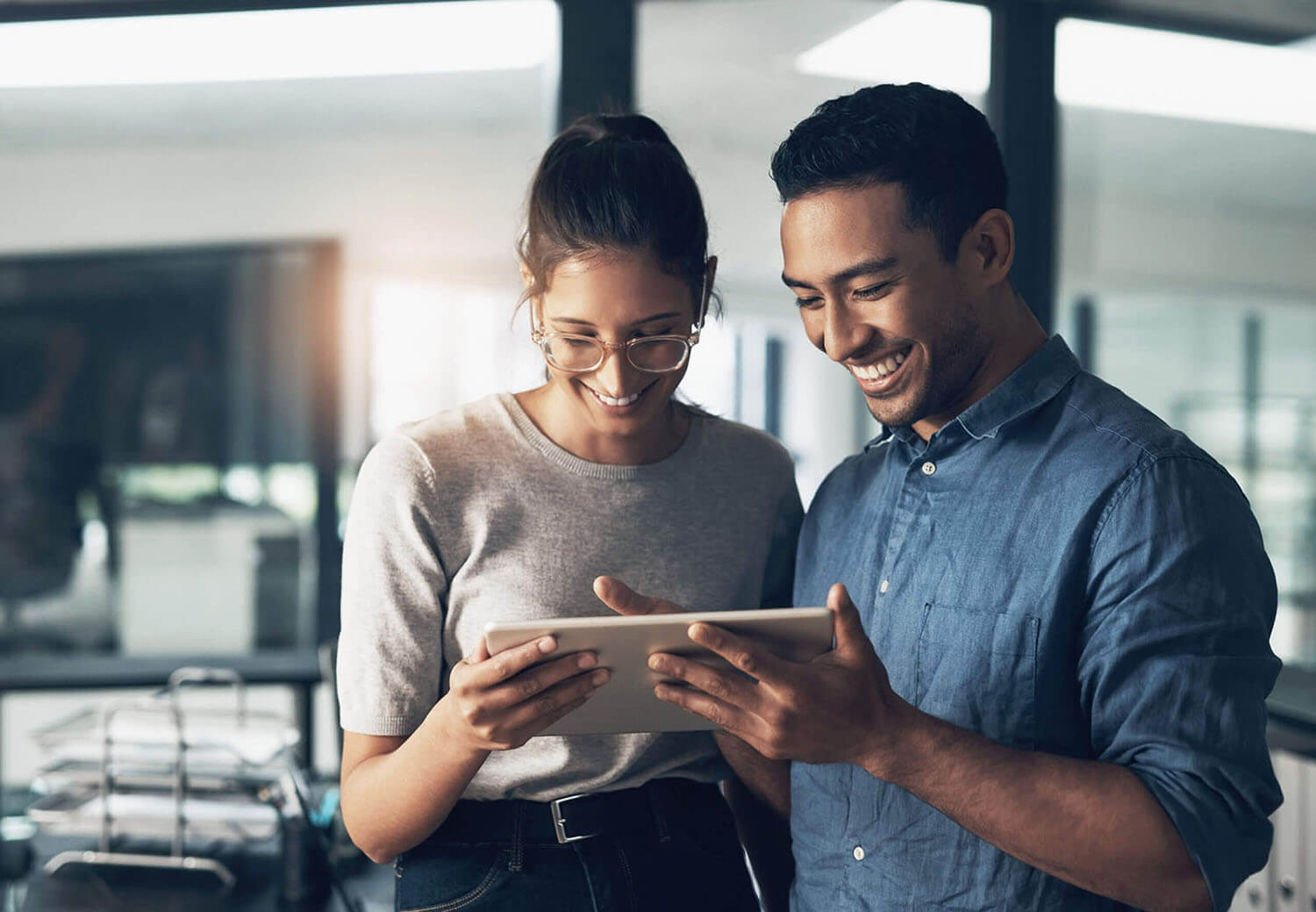 Two young workers look at a tablet, smiling