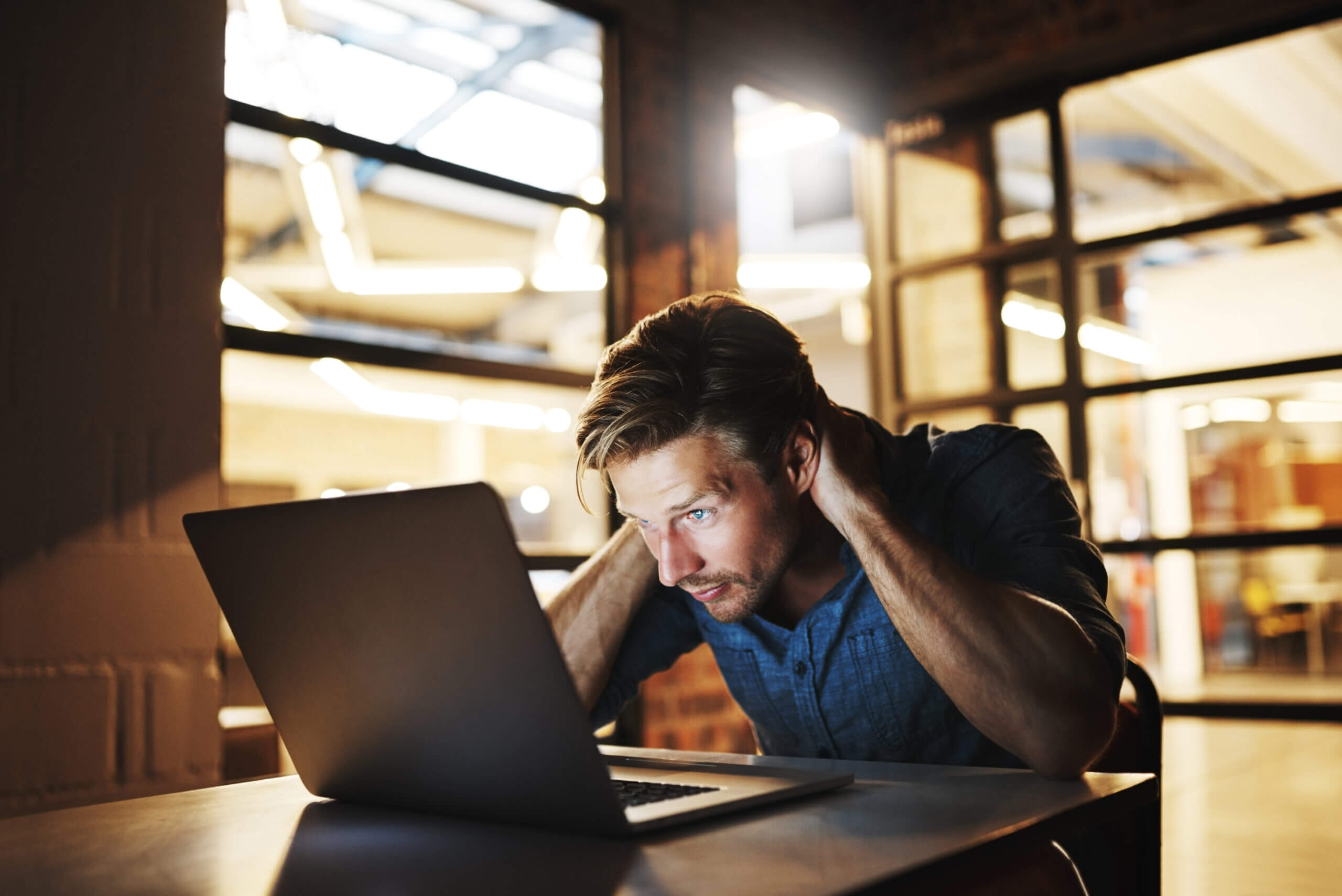 Man looks frustratedly at computer while in an office at night