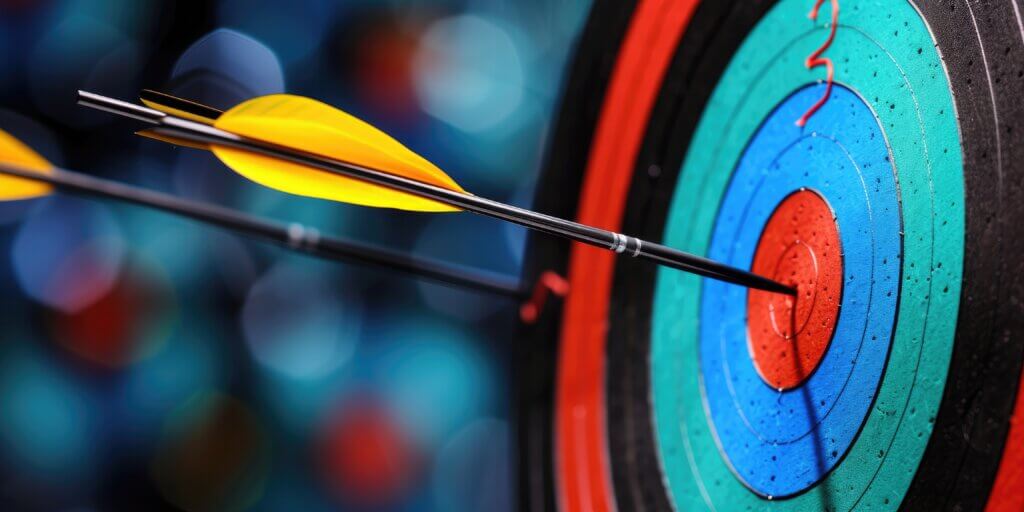 A close-up of two arrows hitting the center bullseye on a colorful target, with a blurred background emphasizing the precision of the darts’ placement