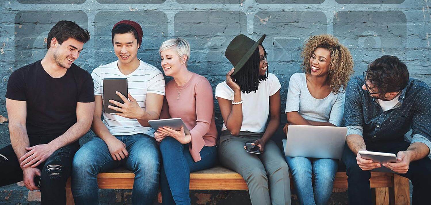 group of cheerful creative businesspeople using their digital devices while sitting on a bench together outdoors