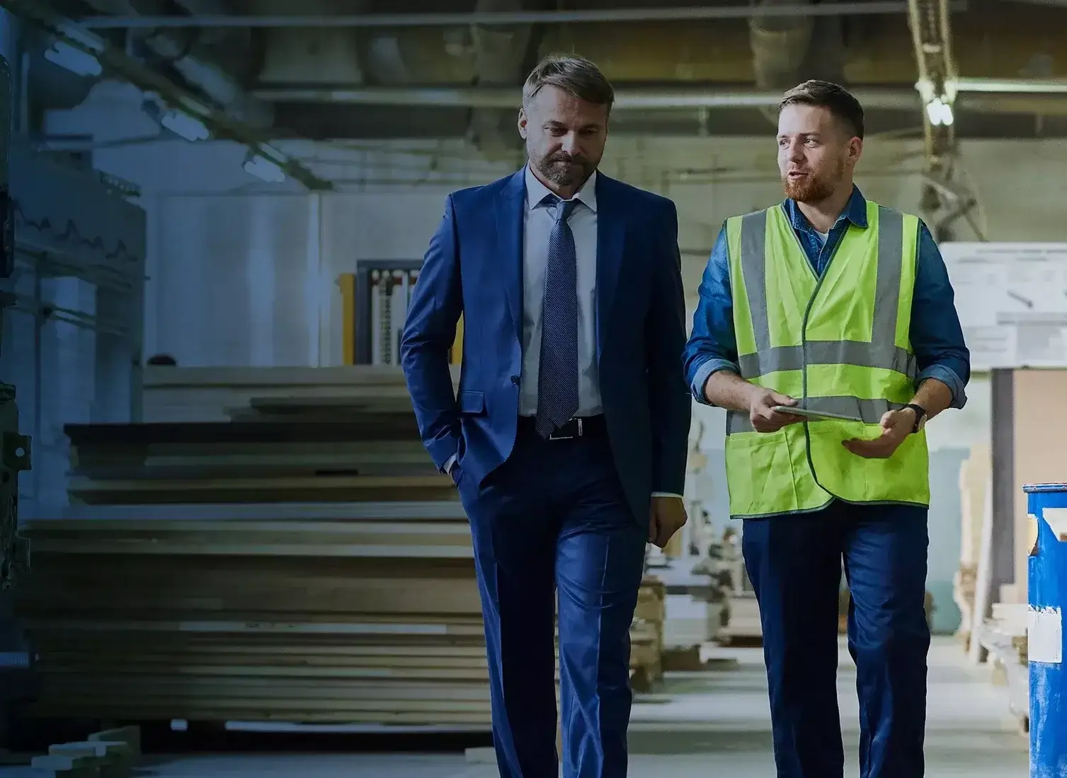 Two men walking in a lumber warehouse talking.