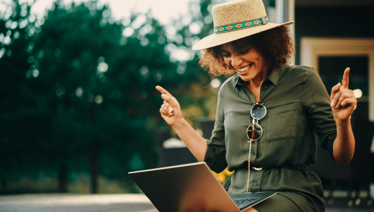 woman in a hat with a laptop pointing her fingers to the sky