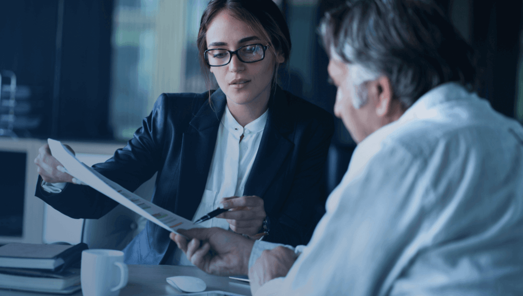 woman with glasses showing a man something on a piece of paper in an office