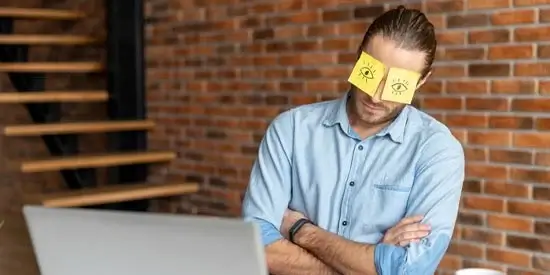 A man sleeping at his desk with sticky notes covering his eyes.