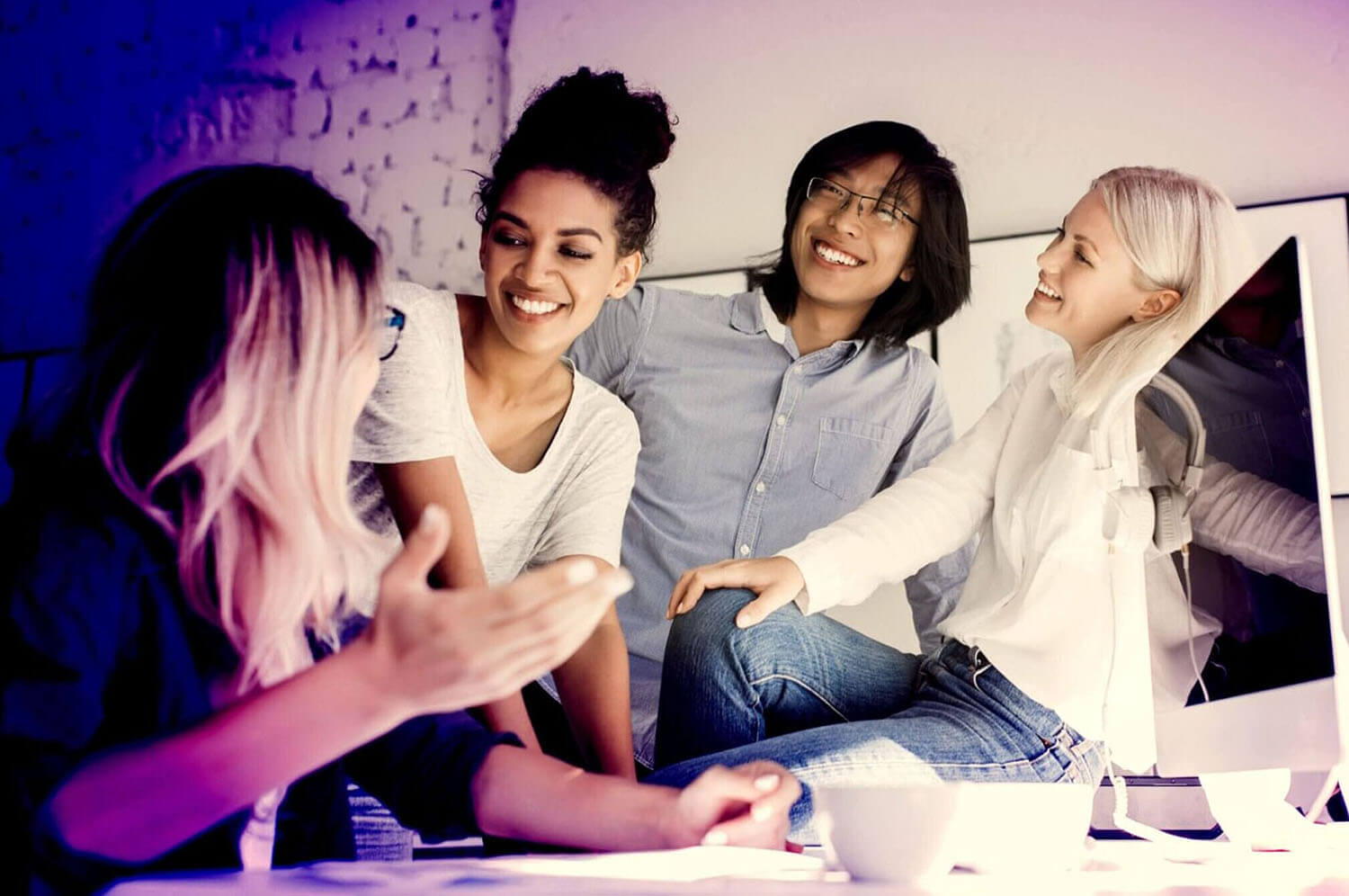 group of young coworkers laughing around computer