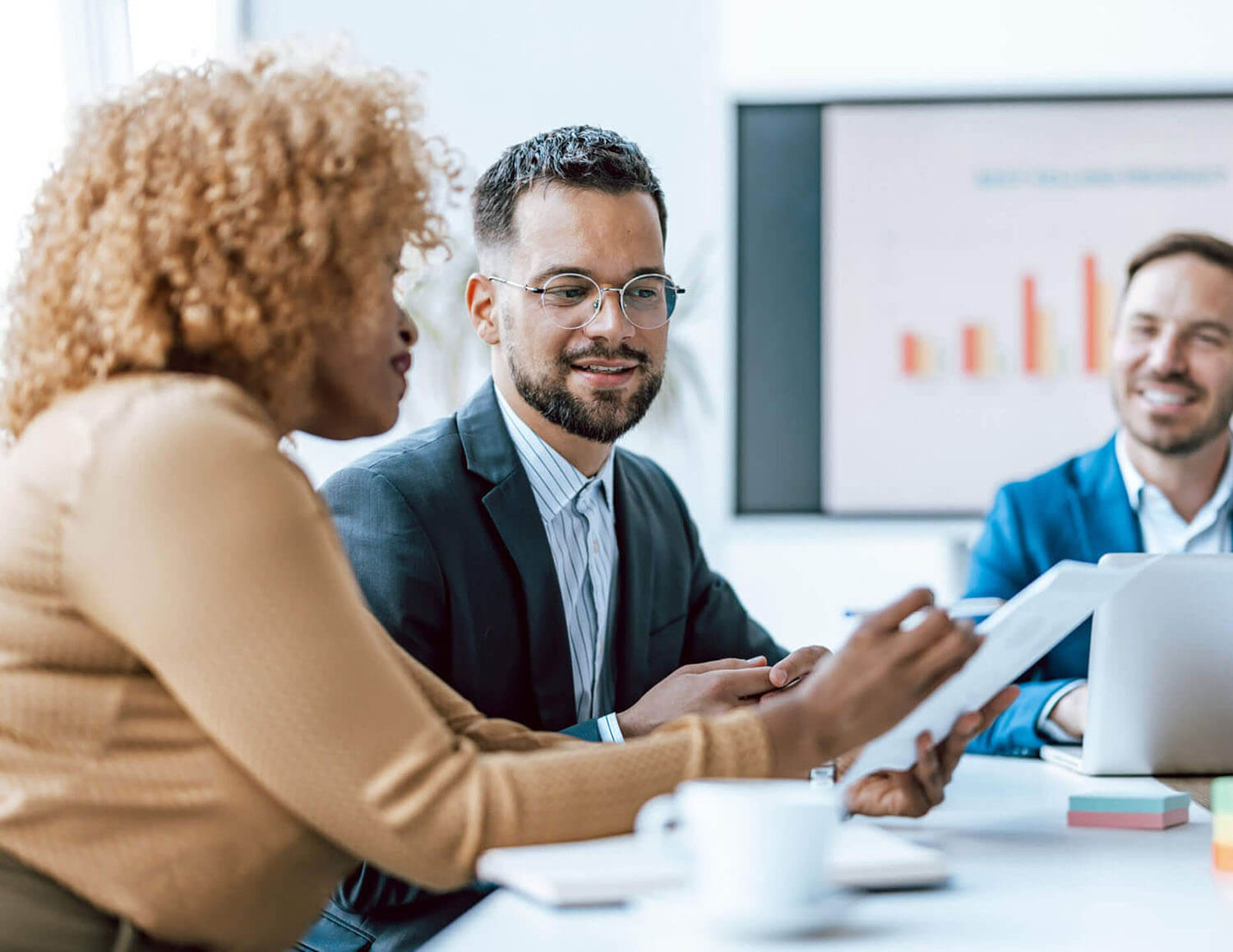 Three professionals are engaged in a business meeting with one man presenting a digital tablet showcasing work-related content