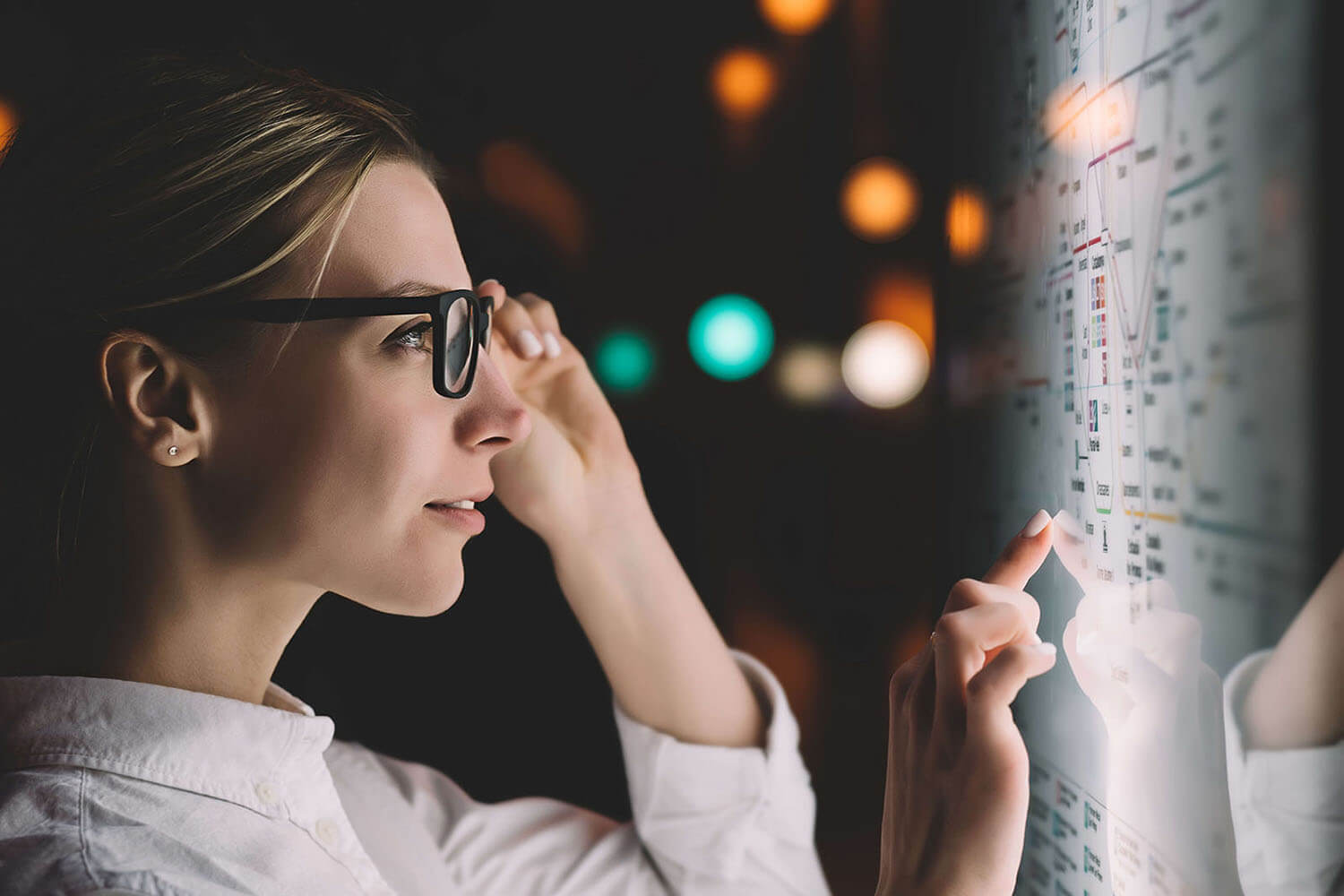 Woman stands in front of a giant display screen of data, adjusting her glasses