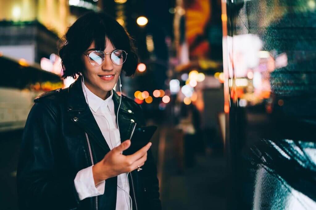 Woman walks the street at night looking at her phone