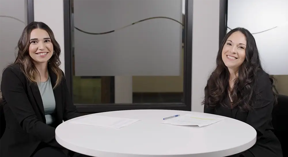 Two women smiling sitting at conference table