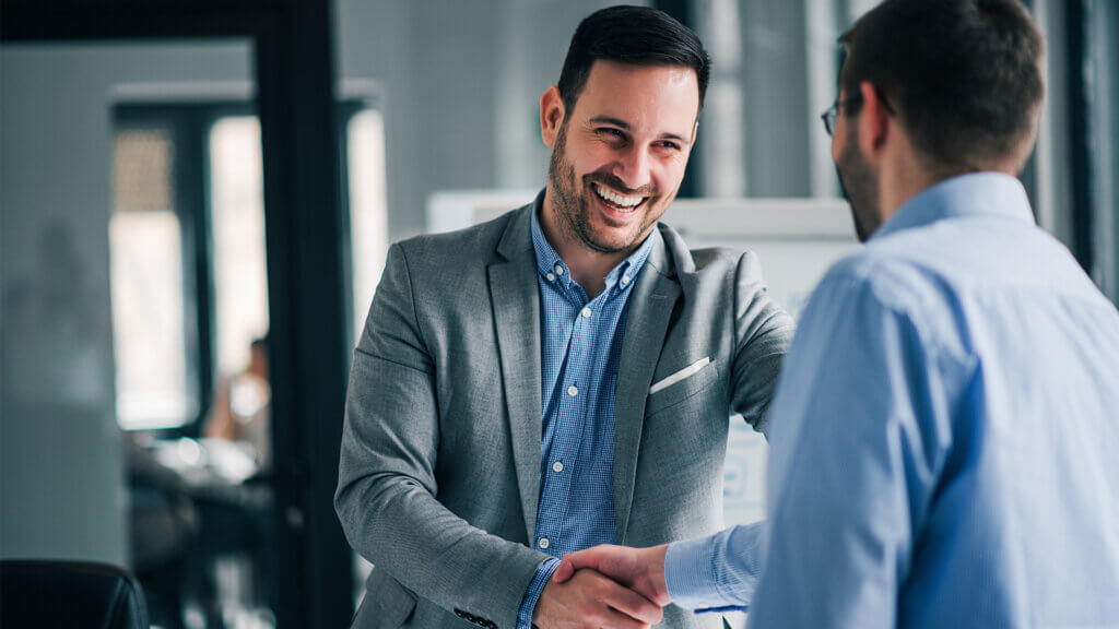 Two men in business attire shaking hands in an office setting.