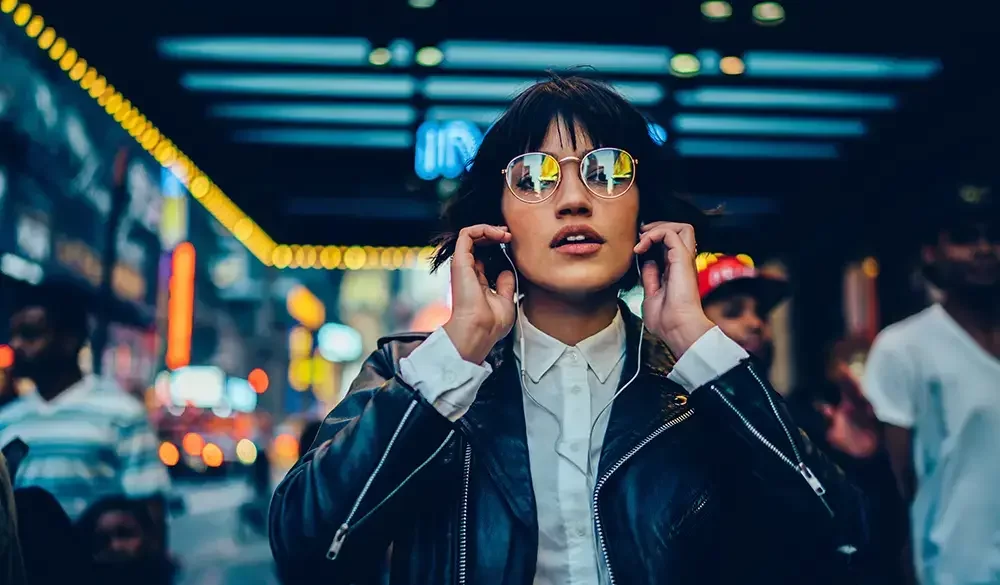 girl with glasses and headphones walking through crowded area