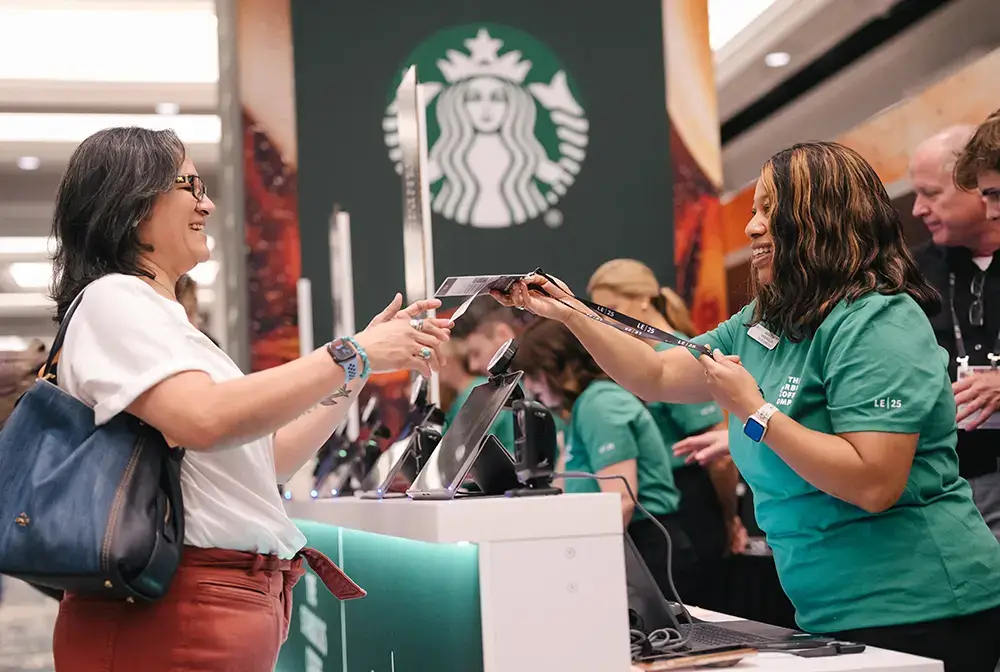 woman at event registration counter handing a badge to attendee