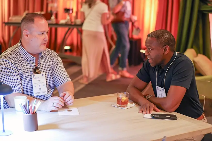 Two men sitting at a table and talking at an event